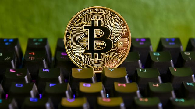 A physical gold bitcoin coin standing upright on a backlit mechanical keyboard — Ronin's Karst upgrade goes live October 7 and the 0.0637 line decides the next move in RON