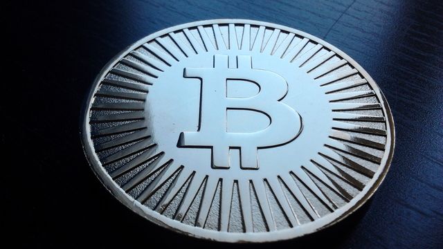 A physical mock bitcoin challenge coin on a dark blue surface — bitcoin's $6,606 October slide wiped out $1.16 billion of leveraged longs