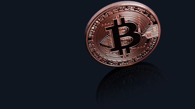 A physical Bitcoin coin on a dark reflective surface — spot Bitcoin ETF outflows in October 2026