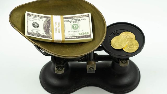 Bitcoin medallions weighed against a stack of US dollar bills — the Fed rate hike, the CLARITY Act defeat and the $76,700 line that decides Bitcoin's next move