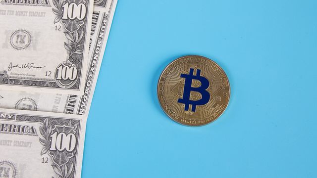 A gold physical bitcoin token beside US hundred-dollar bills on a blue surface — the XRP Faucet pays 0.15 XRP every 15 minutes, $18.76 a day at $1.303 and a $20 payout on claim 103