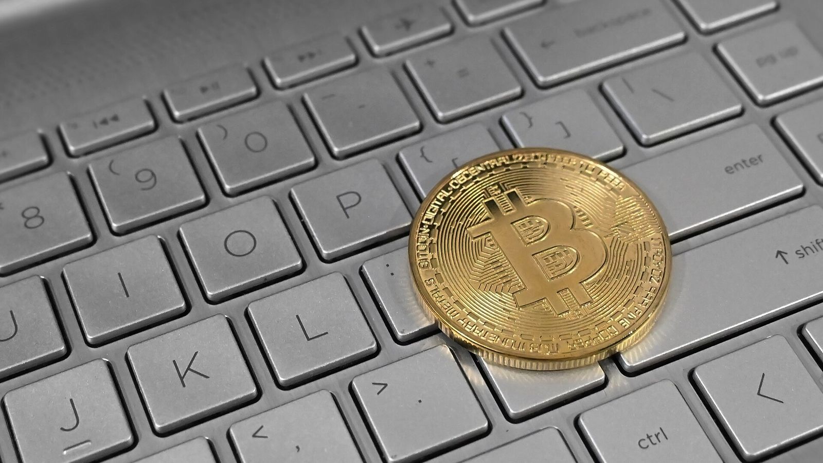 A physical bitcoin resting on a laptop keyboard — the EarnCrypto video library with twenty filmed walkthroughs of crypto earning tools