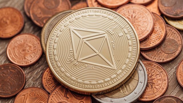 A close-up of a physical Ethereum coin resting on a pile of fiat coins — Arbitrum's ARB token re-rating as Standard Chartered opens coverage with a $10 price target for 2030