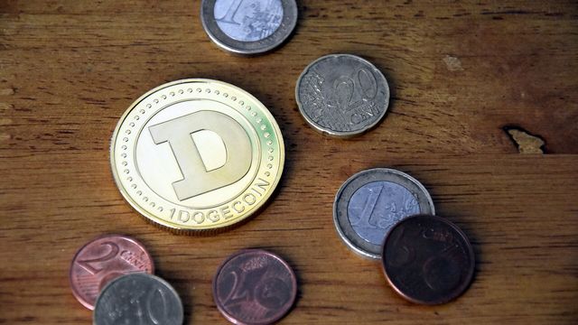A gold physical Dogecoin coin engraved with the D mark among euro coins on a wooden table — Dogecoin Faucet review, 0.3 DOGE every 15 minutes