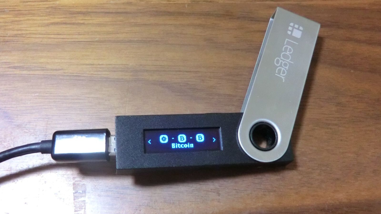 A powered-on Ledger Nano S hardware wallet connected by cable on a wooden desk - Ethereum's EIP-7906 would let a wallet revert a transaction whose outcome does not match the rule it signed
