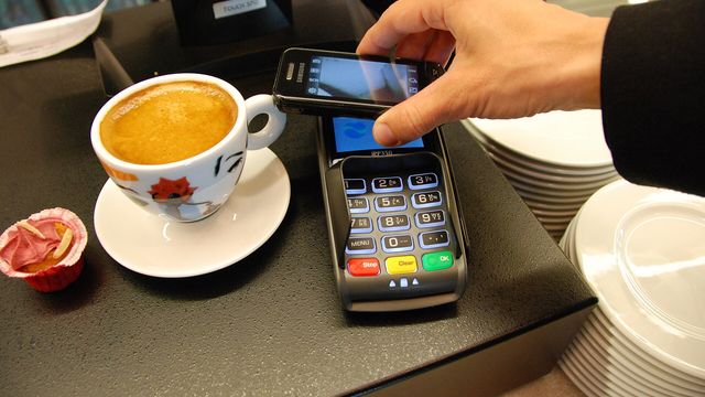 A phone tapped on a card payment terminal at a cafe counter — Mastercard Agent Pay for Machines lets AI agents settle USDC on Base