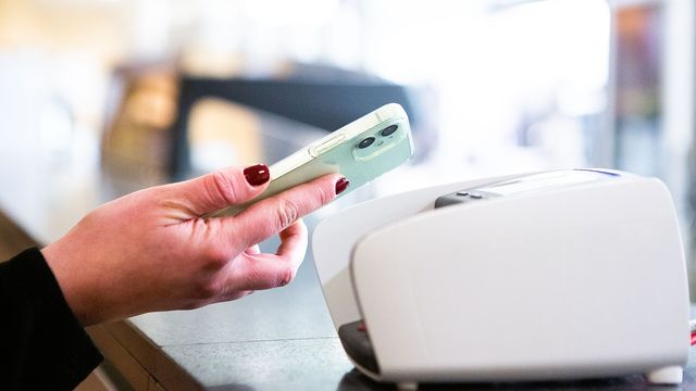 A hand tapping a smartphone on a contactless card payment terminal — Ethena ENA unlock and USDe buyback