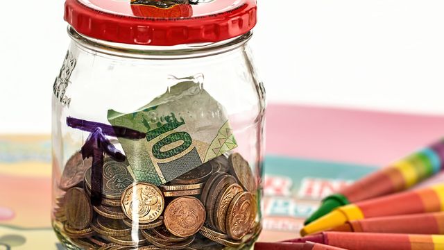 A glass jar piggy bank filled with coins and a banknote - Little Piggie Tales crypto slot free daily claim
