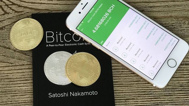 A mobile phone showing a Bitcoin Cash wallet next to a printed Bitcoin whitepaper — the CME BCH futures listing and the pending Grayscale BCH ETF conversion