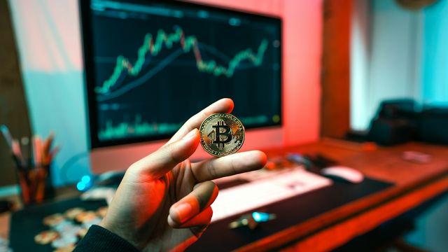 A person holding a crypto coin in front of a computer — GNOT, the Gno.land network token, listing on KuCoin and Kraken on September 16